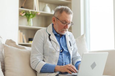 Dizüstü bilgisayarla çalışan kıdemli doktor. Profesyonel yetişkin sağlık uzmanı bilgi arıyor ya da hastane odasında online danışmanlık yapıyor. Tıbbi sağlık hizmetleri sağlık kontrolü