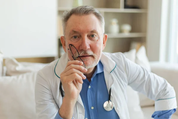 Mature senior male doctor in glasses medical uniform smiling looking at camera in hospital. General practitioner GP therapist professional healthcare expert in clinic. Healthcare concept
