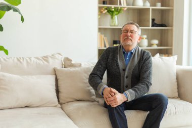 Diz ağrısı, eklem iltihabı, vücut hastalıkları, sağlık hizmetleri. Evdeki kanepede oturan mutsuz, orta yaşlı, diz ağrısı çeken bir adam. Yaşlı büyükbaba bacağına dokunuyor ve dizinde ağrı hissediyor.