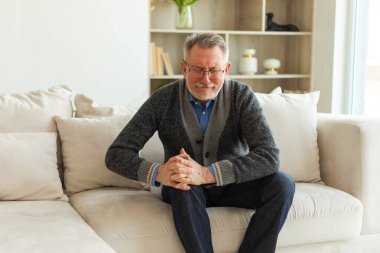Diz ağrısı, eklem iltihabı, vücut hastalıkları, sağlık hizmetleri. Evdeki kanepede oturan mutsuz, orta yaşlı, diz ağrısı çeken bir adam. Yaşlı büyükbaba bacağına dokunuyor ve dizinde ağrı hissediyor.