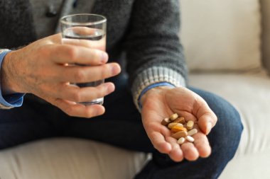 Haplı eller. Yaşlı adam ellerinde tıbbi hap ve bir bardak su tutuyor. Olgun yaşlı büyükbaba ilaç tedavisi hapları alıyor vitamin. Yaş reçeteli ilaç sağlık tedavisi kavramı