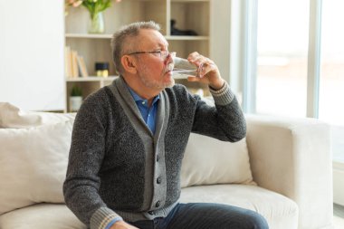 Evde bardak tutan kıdemli adam tatlı su içiyor. Olgun, yaşlı, yaşlı, susamış büyükbaba sağlığıyla ilgilenir. Sağlık hizmeti su dengesi. Yaşlı sağlıklı yaşam tarzı