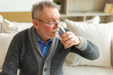 Evde bardak tutan kıdemli adam tatlı su içiyor. Olgun, yaşlı, yaşlı, susamış büyükbaba sağlığıyla ilgilenir. Sağlık hizmeti su dengesi. Yaşlı sağlıklı yaşam tarzı