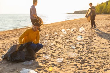 Dünya günü. Gönüllü eylemciler sahil bölgesindeki çöpleri topluyor. Kadınlar ve erkekler okyanus kıyısındaki çöp torbasına plastik çöp koyar. Çevre koruma kıyı bölgesi temizliği