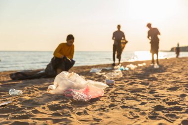 Dünya günü. Gönüllü eylemciler sahil bölgesindeki çöpleri topluyor. Kadınlar ve erkekler okyanus kıyısındaki çöp torbasına plastik çöp koyar. Çevre koruma kıyı bölgesi temizliği