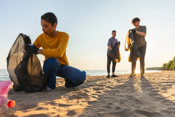 地球の日 ボランティア活動家は ビーチ沿岸地域のゴミ洗浄を集めている 女性とマンは 海岸のゴミ袋にプラスチックごみを入れています 環境保全の沿岸地域のクリーニング — ストック写真