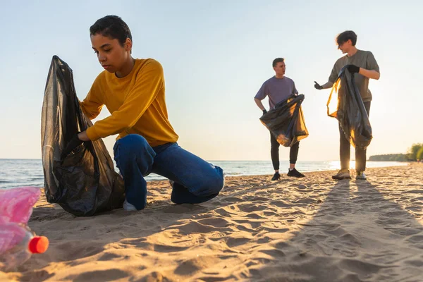 stock image Earth day. Volunteers activists collects garbage cleaning of beach coastal zone. Woman and mans puts plastic trash in garbage bag on ocean shore. Environmental conservation coastal zone cleaning