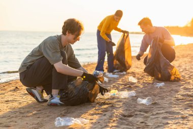 Dünya günü. Gönüllü eylemciler, sahil bölgesindeki çöpleri topluyor. Bir grup insan okyanus kıyısındaki çöp torbalarına plastik çöp koyuyor. Çevresel koruma
