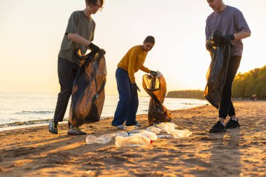Dünya günü. Gönüllü eylemciler sahil bölgesindeki çöpleri topluyor. Kadınlar ve erkekler okyanus kıyısındaki çöp torbasına plastik çöp koyar. Çevre koruma kıyı bölgesi temizliği