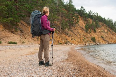 Turizm macerası yürüyüşü. Gezgin kadın güzel manzaraya bakıyor. Sırt çantalı gezgin bayan turist göl kenarında yürüyor. Genç ve mutlu bir kadın aktif turizm gezintisinin tadını çıkarıyor.