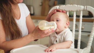 Evde mutlu bir aile. Anne, küçük bebeğini mutfaktaki şişeden besliyor. Yeni doğmuş kız süt içiyor. Bebek emziriyor, süt yiyor ve sandalyeye oturuyor. Bebeği emziren anne.