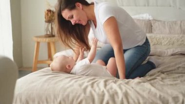 Evde mutlu bir aile. Anne, küçük bebekle yatakta oynuyor. Anne bebek birlikte oynayıp rahatlıyor. Anne bebeğe sevgiyle bakar. Bebeği emziren anne oturma odasında dinleniyor.