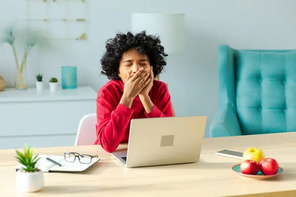 Sleepy african american woman sitting at table with laptop and yawning. Tired overworked girl lazy to work. Student businesswoman relaxing bored in home office after work on laptop computer