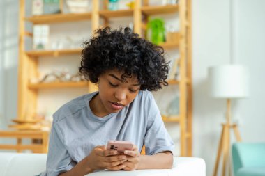 African girl holding smartphone touch screen typing scroll page at home. Woman with cell phone surfing internet using social media apps playing game. Shopping online Internet news cellphone addiction