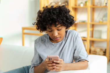 African girl holding smartphone touch screen typing scroll page at home. Woman with cell phone surfing internet using social media apps playing game. Shopping online Internet news cellphone addiction