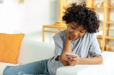 African girl holding smartphone touch screen typing scroll page at home. Woman with cell phone surfing internet using social media apps playing game. Shopping online Internet news cellphone addiction