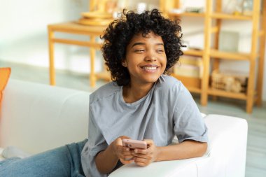 African girl holding smartphone touch screen typing scroll page at home. Woman with cell phone surfing internet using social media apps playing game. Shopping online Internet news cellphone addiction