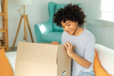 Paketleri açan Afrikalı kız kutuya bakıyor. Kutuyu açan mutlu kadın. Paket teslim edilen eşyalara bakan bir kadın. Tatmin olmuş istemci olumlu geri bildirim hızlı teslimatı