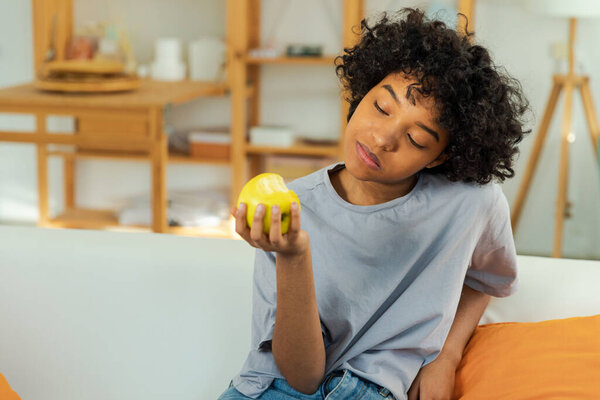 Happy pretty girl biting green apple at home. Beautiful african american young woman eating fresh fruit and smiling. Healthy food vegan vegetarian dieting concept. Healthy snack clean food