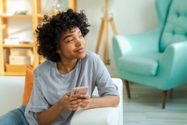 African girl holding smartphone touch screen typing scroll page at home. Woman with cell phone surfing internet using social media apps playing game. Shopping online Internet news cellphone addiction