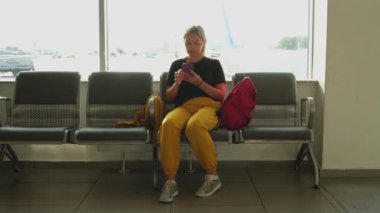Havaalanı terminali. Akıllı telefon kullanan bir kadın uçuşu bekliyor. Havaalanında cep telefonlu bir kız internet sosyal medya uygulamalarında sörf yapıyor. Havayolu merkezinin pansiyonunda seyahat eden bir kadın. Gezgin kız.