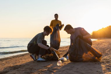 Dünya günü. Gönüllü eylemciler sahil bölgesindeki çöpleri topluyor. Kadınlar ve erkekler okyanus kıyısındaki çöp torbasına plastik çöp koyar. Çevre koruma kıyı bölgesi temizliği