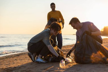 Dünya günü. Gönüllü eylemciler sahil bölgesindeki çöpleri topluyor. Kadınlar ve erkekler okyanus kıyısındaki çöp torbasına plastik çöp koyar. Çevre koruma kıyı bölgesi temizliği