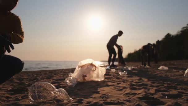 地球の日 ボランティア活動家は ビーチ沿岸地域のゴミ洗浄を集めている 女性とマンは 海岸のゴミ袋にプラスチックごみを入れています 環境保全の沿岸地域のクリーニング — ストック動画