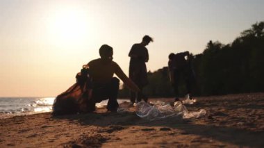Dünya günü. Gönüllü eylemciler sahil bölgesindeki çöpleri topluyor. Kadınlar ve erkekler okyanus kıyısındaki çöp torbasına plastik çöp koyar. Çevre koruma kıyı bölgesi temizliği