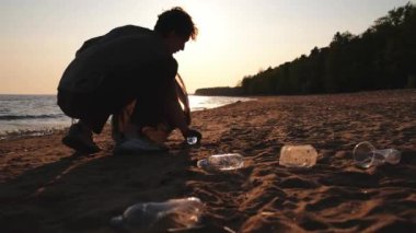 Dünya günü. Gönüllü eylemciler sahil bölgesindeki çöpleri topluyor. Adam okyanus kıyısındaki çöp torbasına plastik çöp koyuyor. Çevre koruma kıyı bölgesi temizliği