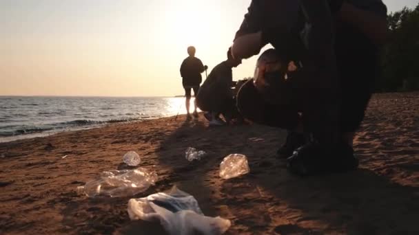 地球の日 ボランティア活動家は ビーチ沿岸地域のゴミ洗浄を集めている マンと女性は 海岸のゴミ袋にプラスチックごみを入れています 環境保全の沿岸地域のクリーニング — ストック動画