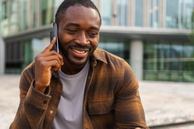 Açık havada, sokakta akıllı telefondan konuşan Afrikalı Amerikalı bir adam. Cep telefonlu bir adam arkadaşlarıyla sohbet ediyor. Gülümseyen kişi cep telefonuyla cevap veriyor. Cep telefonuyla konuşan adam