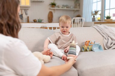 Evde mutlu bir aile. Anne ve bebek evdeki kanepede oyuncaklarla oynuyor. Küçük çocuk ve bebek bakıcısı birlikte eğleniyorlar. Genç kadın, anne, çocuk oturma odasında dinleniyor.