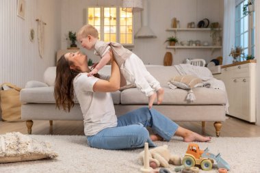 Evde mutlu bir aile. Anne küçük bir çocuğu havadan kaldırıyor. Anne ve bebek evde oyun oynuyorlar. Anne bebeğe sevgiyle sarılır. Küçük anne oğlu oturma odasında dinleniyor.