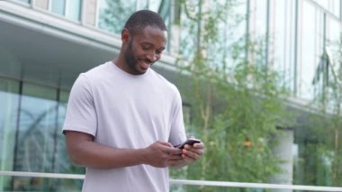 Afro-Amerikan bir adam elinde akıllı telefon, dokunmatik ekranlı parşömen kağıdı tutuyor. Şehir caddesinde. İnternette cep telefonu sörfü yapan bir adam sosyal medya uygulamaları kullanarak internetten alışveriş yapıyor. Cep telefonu bağımlılığı