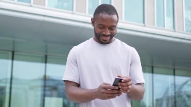 Afro-Amerikan bir adam elinde akıllı telefon, dokunmatik ekranlı parşömen kağıdı tutuyor. Şehir caddesinde. İnternette cep telefonu sörfü yapan bir adam sosyal medya uygulamaları kullanarak internetten alışveriş yapıyor. Cep telefonu bağımlılığı