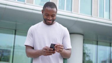 Afro-Amerikan bir adam elinde akıllı telefon, dokunmatik ekranlı parşömen kağıdı tutuyor. Şehir caddesinde. İnternette cep telefonu sörfü yapan bir adam sosyal medya uygulamaları kullanarak internetten alışveriş yapıyor. Cep telefonu bağımlılığı