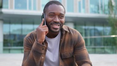 Açık havada, sokakta akıllı telefondan konuşan Afrikalı Amerikalı bir adam. Cep telefonlu bir adam arkadaşlarıyla sohbet ediyor. Gülümseyen kişi cep telefonuyla cevap veriyor. Cep telefonuyla konuşan adam