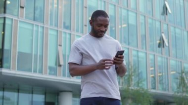 Afro-Amerikalı adam elinde akıllı telefon ekranı ile caddede daktilo yazıyor. Sosyal medya uygulamaları kullanarak internette cep telefonu sörfü yapan bir adam. İnternet üzerinden haber alışverişi cep telefonu bağımlılığı
