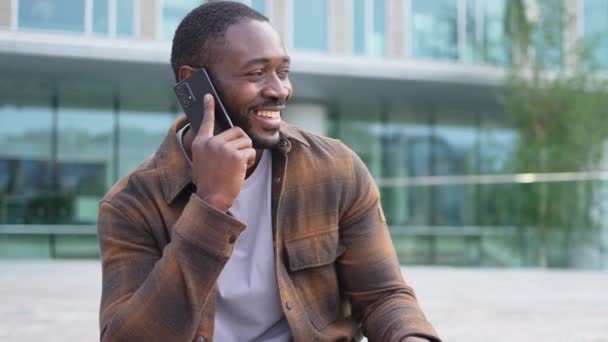 非洲裔美国人在城市户外的街上用智能手机交谈 拿着手机和朋友聊天的男人 笑着用手机接听电话的人 用手机聊天的人 — 图库视频影像