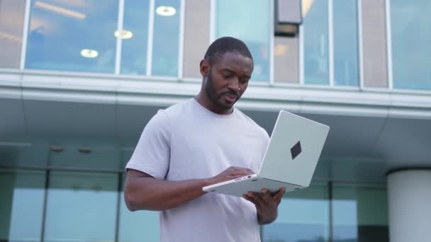 アフリカ系アメリカ人のフリーランサーは 都市の街頭でラップトップのタイピングを使用しています バーチャルミーティング オンラインチャット会議 屋外でラップトップに取り組む起業家プログラマー リモートワーク — ストック動画