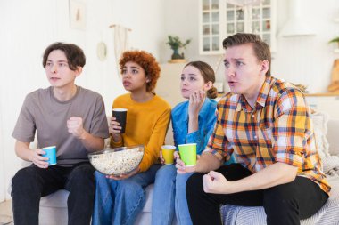 Bir grup arkadaş televizyonda futbol maçı izliyorlar. Memlekette zaferi kutlayan futbol taraftarları. Arkadaşlık sporu eğlence konsepti. Çeşitli arkadaşlar evde birlikte eğleniyorlar.