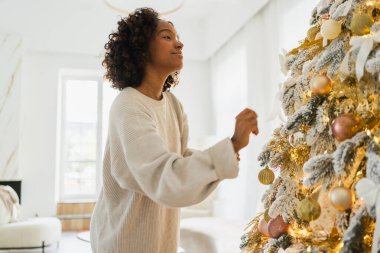 Mutlu noeller. Noel ağacı süsleyen Afrikalı Amerikalı kadın. Klasik Noel ağacının yanında beyaz gümüş süslemeleri olan mutlu bir kız. Noel arifesinde evde kutlama zamanı.
