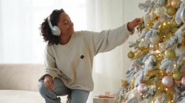 Mutlu noeller. Kulaklık takan Afrikalı Amerikalı bir kadın Noel ağacı süsleme müziği dinliyor. Klasik Noel ağacının yanında mutlu bir kız. Noel arifesinde evde kutlama zamanı.