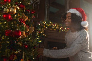 Mutlu noeller. Noel ağacı süsleyen Afrikalı Amerikalı kadın. Klasik kırmızı altın süslemeli geleneksel Noel ağacının yanında mutlu bir kız. Noel arifesinde evde kutlama zamanı.