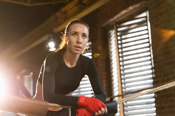 Woman fighter girl power. Woman fighter with red boxing wraps protective bandages standing on boxing ring leaning on ropes waiting resting. Strong powerful girl. Strength fit body workout training