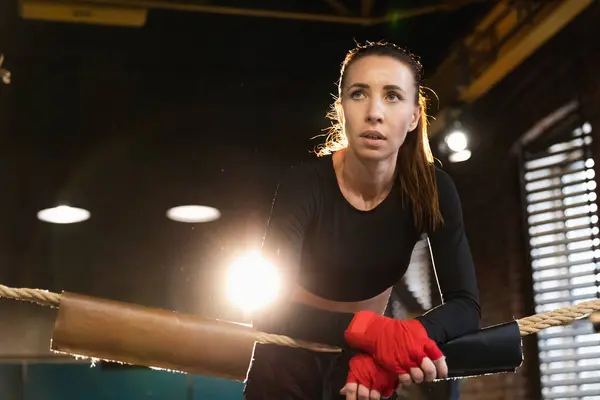 Woman fighter girl power. Woman fighter with red boxing wraps protective bandages standing on boxing ring leaning on ropes waiting resting. Strong powerful girl. Strength fit body workout training