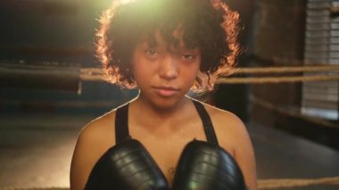 Bağımsız kız gücü diye bağır. Boks eldivenli kızgın Afrikalı Amerikalı kadın dövüşçü boks ringinde kameraya karşı oldukça agresif görünüyor. Güçlü ve güçlü bir kız.