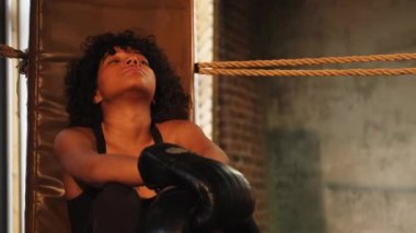 Savaşçı kadın gücü. Boks eldivenli Afrika kökenli Amerikalı kadın boksör boks ringinde oturmuş, kavgadan sonra dinleniyor. Spor salonunda güçlü bir kız. Vücut çalıştırma eğitimine uygun güç