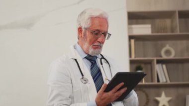 Klinikte dijital tablet kullanan kıdemli erkek doktor. Profesyonel terapist sağlık uzmanı hastane odasında internette bilgi arıyor. Tıbbi sağlık hizmetleri sağlık kontrolü